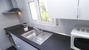 A modern kitchen with a stainless steel sink, a microwave, and a window with a view of greenery outside.