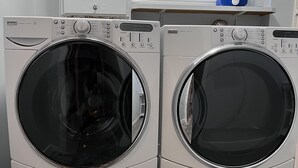 Two front-loading washing machines in a laundry room with a window and a blue water heater in the background. - Calgary elegant single room &shared bathroom close LRT&free parking (Calgary)