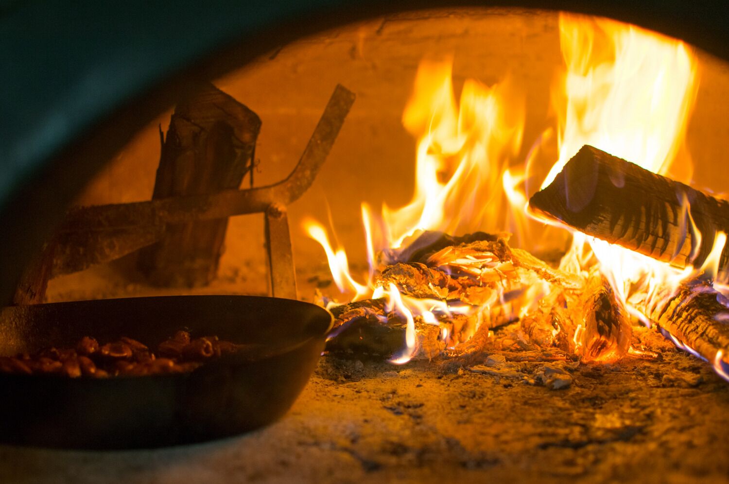 Un forno a legna con ardenti tronchi e una pentola di cibo.