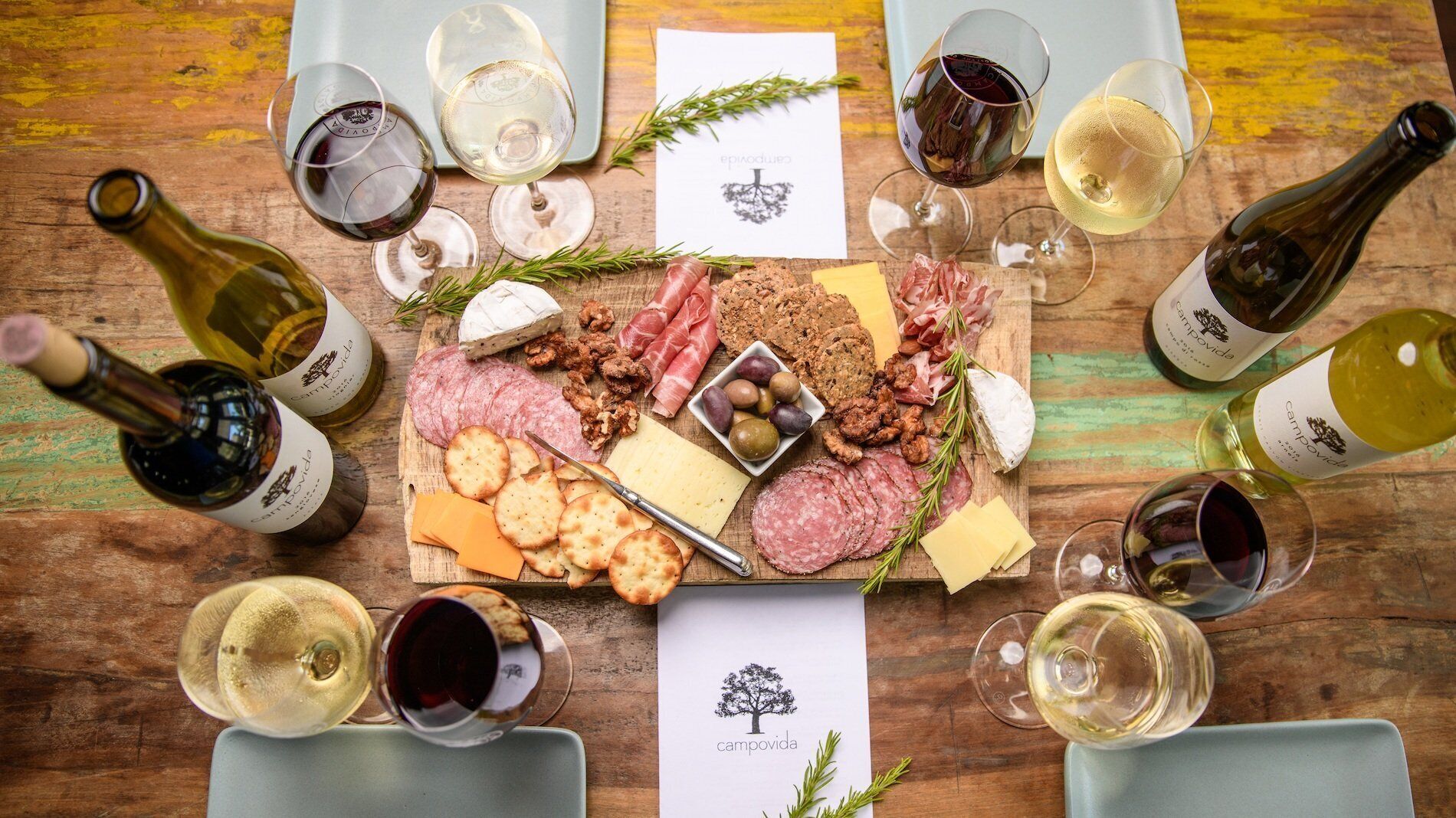A wooden table with a charcuterie board, wine glasses, and bottles of wine.