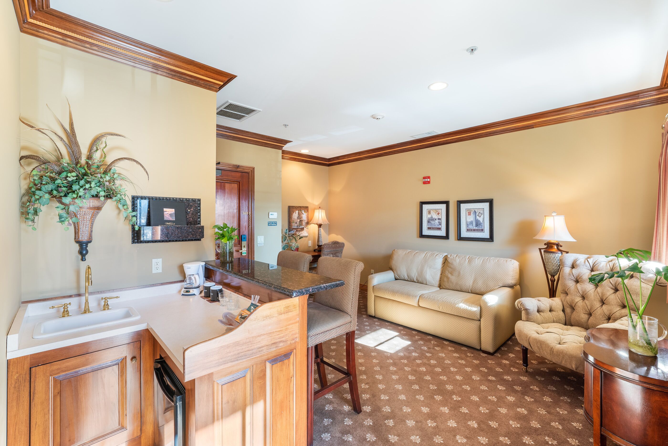 A hotel room with a kitchen area, a sofa, and a dining table.