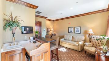 A hotel room with a kitchen area, a sofa, and a dining table.