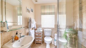 A modern bathroom with a glass shower enclosure, a freestanding bathtub, a toilet, and a sink with a glass shelf. - Downland House - Four Bedroom House, Sleeps 10 (Woolacombe)