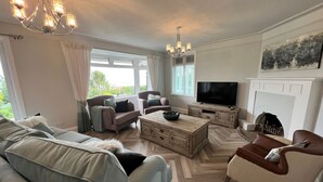 A living room with a sofa, armchairs, a coffee table, a TV, and a fireplace. - Downland House - Four Bedroom House, Sleeps 10 (Woolacombe)