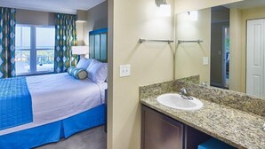 Habitación de hotel con cama, baño con lavamanos y espejo, y ventana con cortinas.