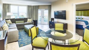 Una habitación de hotel moderna con sofá, una mesa de comedor de cristal y televisor montado en la pared.