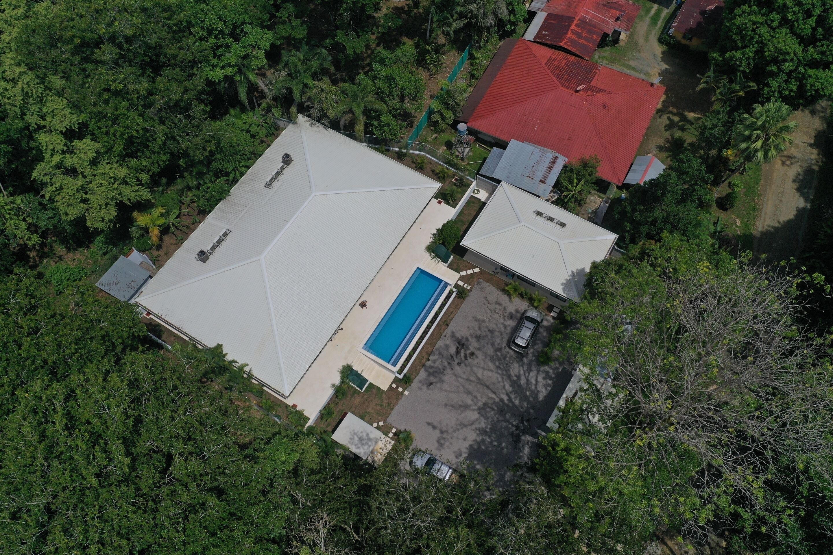 Vista aérea de um bairro residencial com piscina, duas casas com telhados vermelhos e vegetação ao redor.