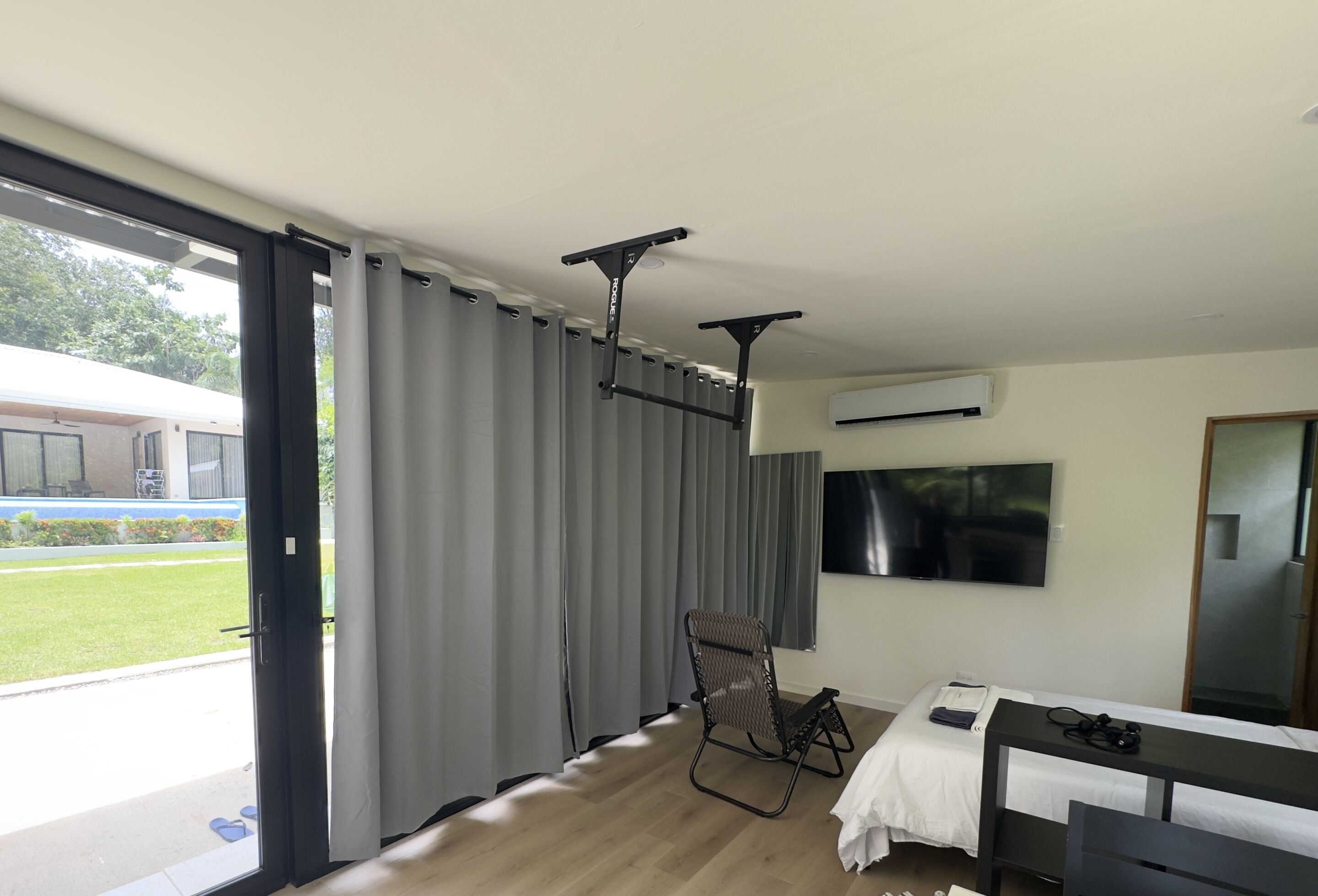Habitación de hotel con cama, una silla, televisor montado en la pared y puerta corrediza de vidrio que da a un espacio al aire libre.