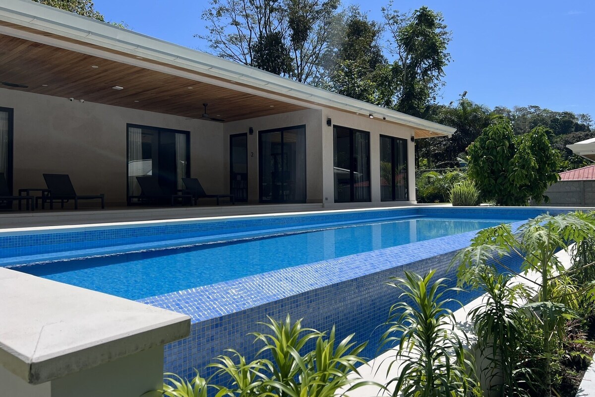 Un espace moderne aménagé au bord de la piscine, avec une piscine à l’eau cristalline, des chaises longues et un patio couvert.