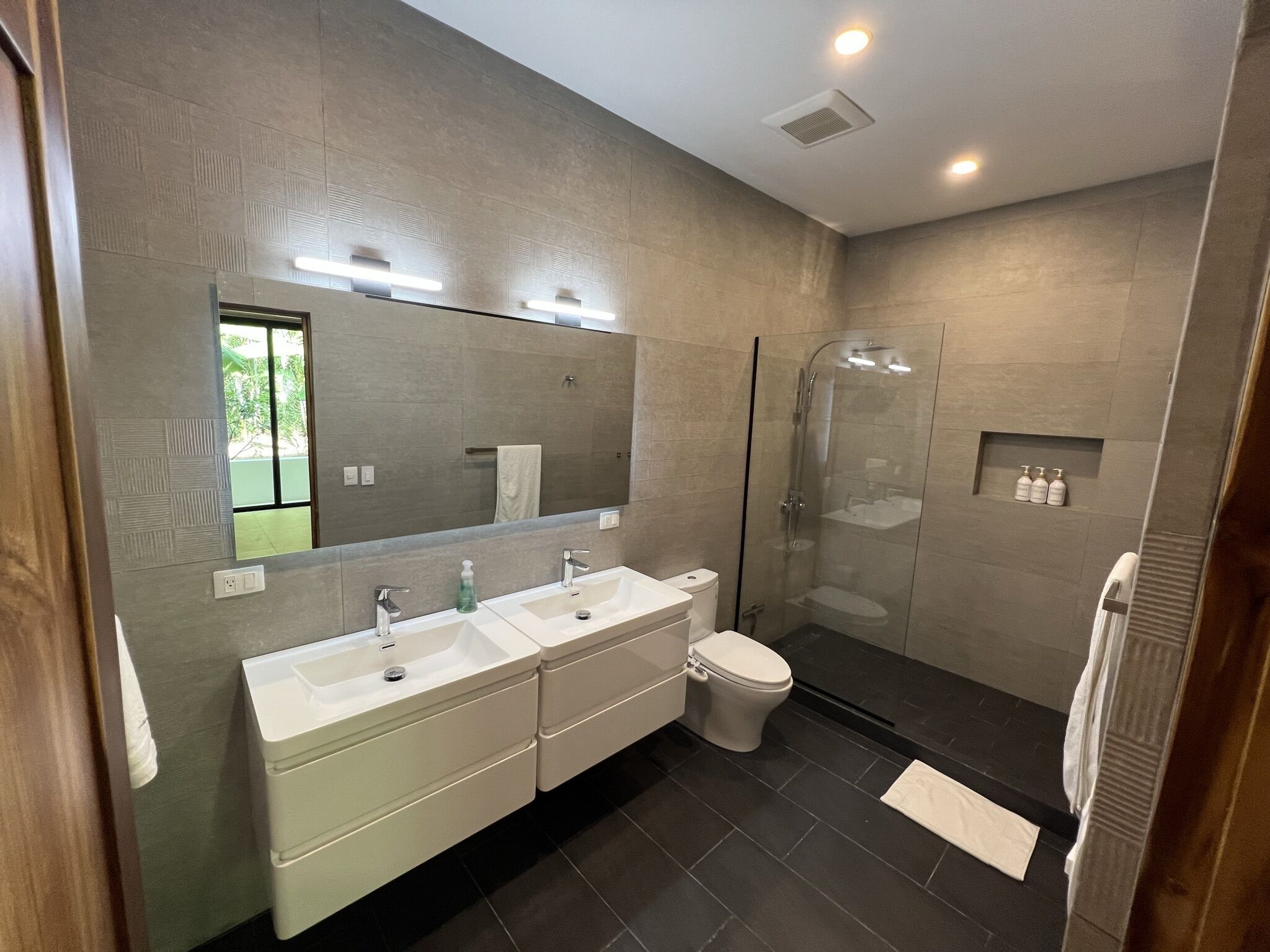 Een moderne badkamer met twee wastafels, een toilet, een douche met glazen wand en een grote spiegel.