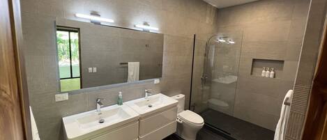 Een moderne badkamer met twee wastafels, een toilet, een douche met glazen wand en een grote spiegel.