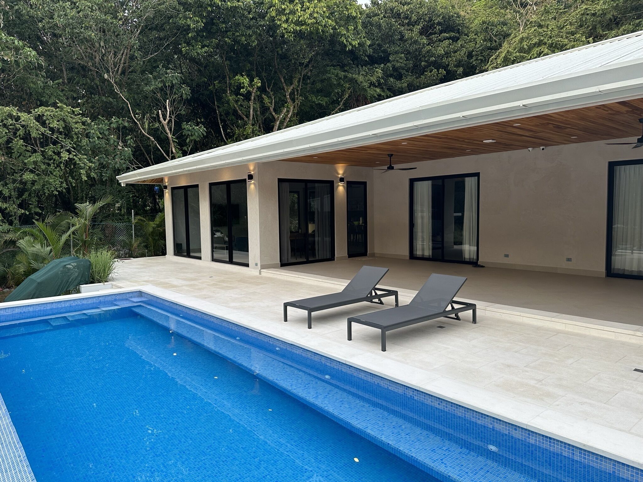 Una casa moderna con piscina, dos sillones de descanso y un patio cubierto.
