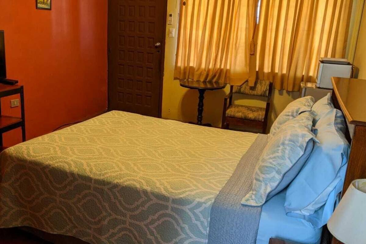 Une chambre d’hôtel avec un lit, un téléviseur posé sur un meuble, une petite table et une chaise.