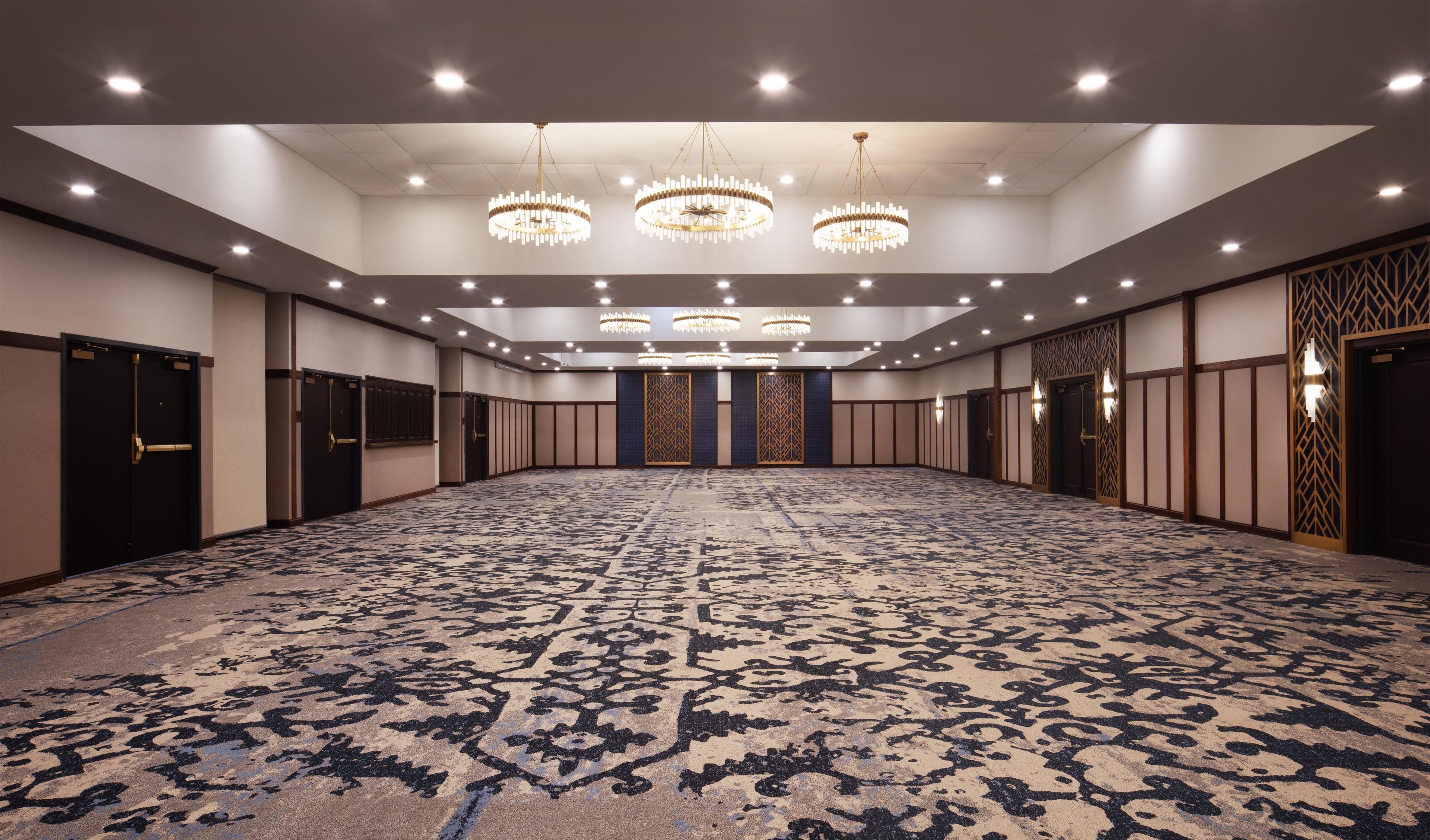 A large conference room with a patterned carpet, multiple chandeliers, and a row of doors on one side.