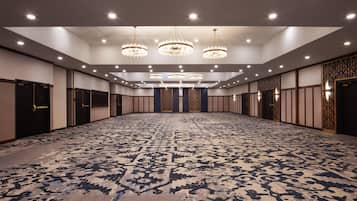 A large conference room with a patterned carpet, multiple chandeliers, and a row of doors on one side.
