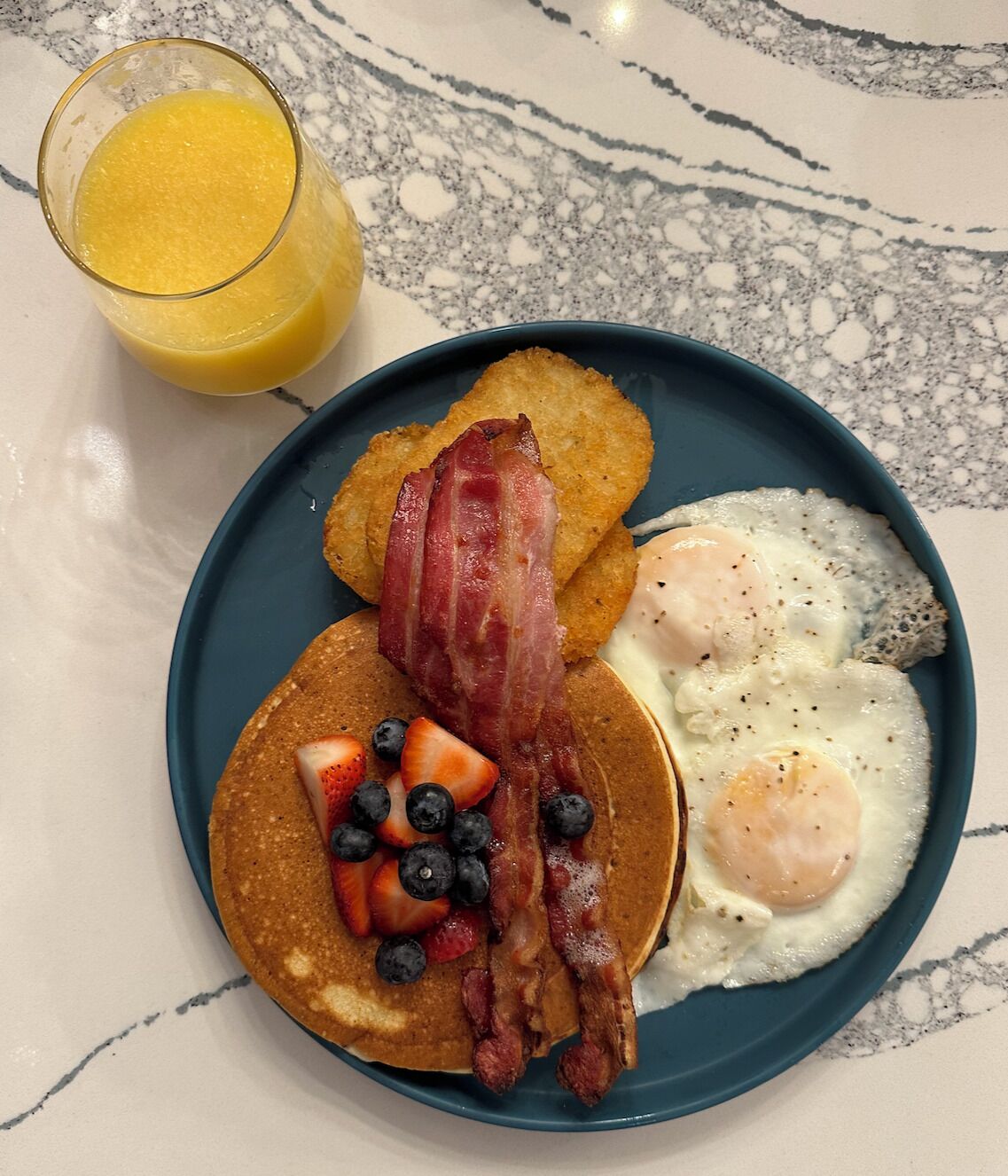 A breakfast plate with pancakes, bacon, eggs, and fruit.