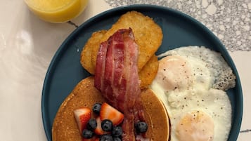 A breakfast plate with pancakes, bacon, eggs, and fruit.