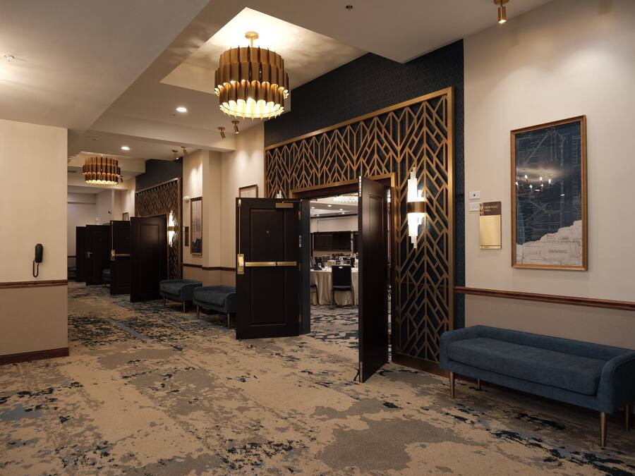 A hotel lobby with a patterned carpet, a blue sofa, a chandelier, and a wall-mounted map.