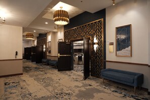 A hotel lobby with a patterned carpet, a blue sofa, a chandelier, and a wall-mounted map. -  Hotel Royer Urbana Champaign, Tapestry Collection by Hilton (Urbana)