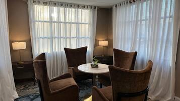 Une chambre d’hôtel avec une table ronde, deux chaises marron, une petite plante et deux lampes.