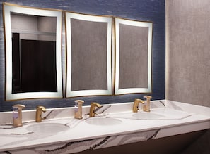 A bathroom with a triple vanity, three gold faucets, and a marble countertop. - Hotel Royer Urbana Champaign, Tapestry Collection by Hilton (Urbana)