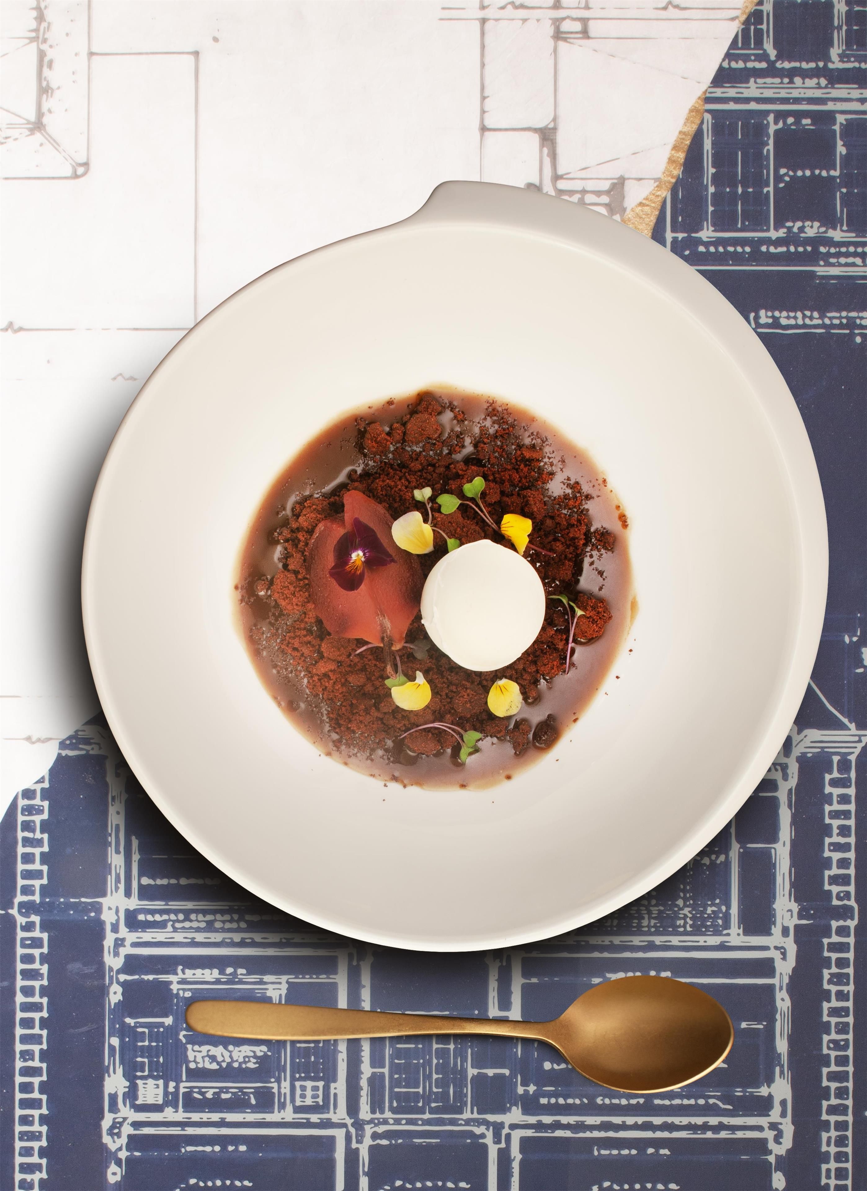 A white plate with a dessert, a spoon, and a patterned tablecloth.