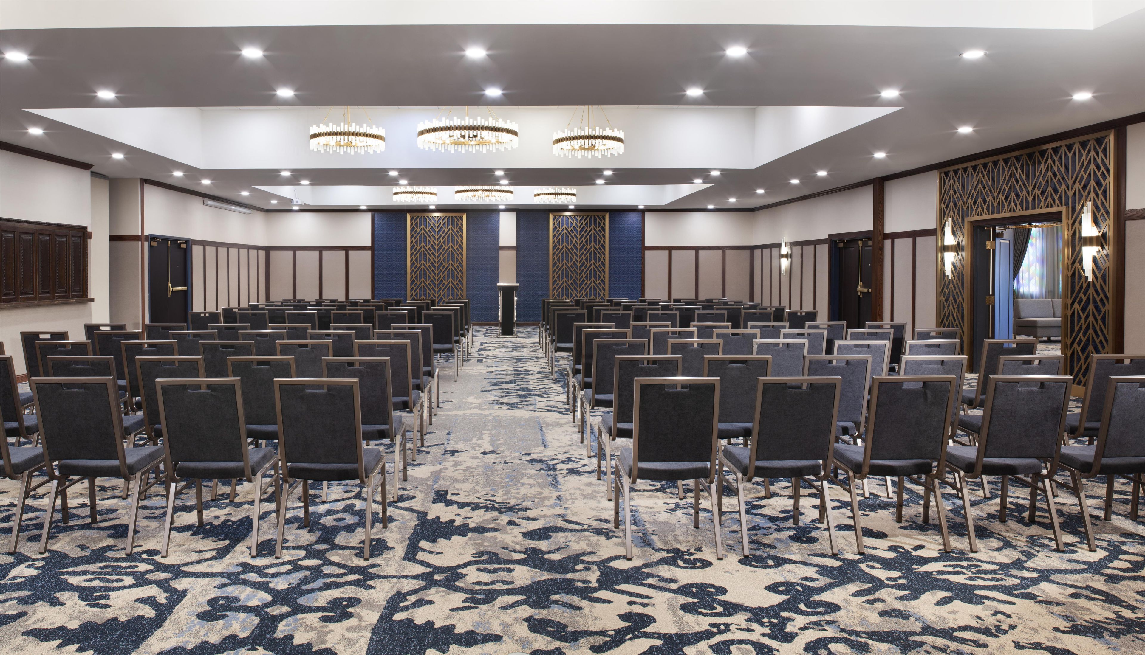 A conference room with rows of chairs, a patterned carpet, and chandeliers.