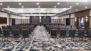 A conference room with rows of chairs, a patterned carpet, and chandeliers.