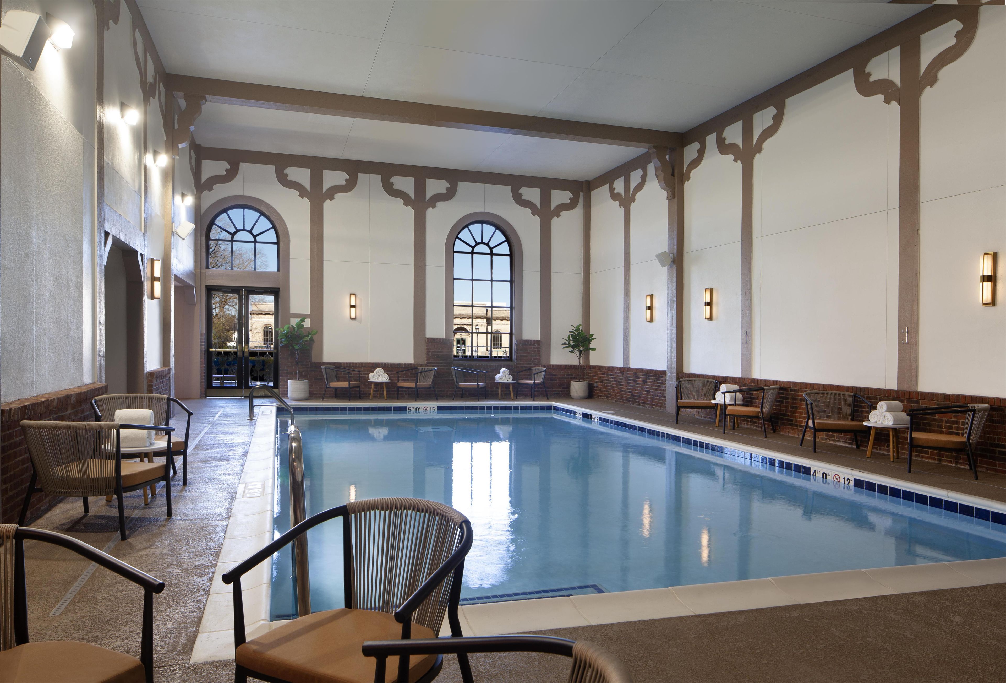 Piscina interior con una vista despejada del área, incluyendo el borde de la piscina, sillas circundantes y una puerta que da al exterior.