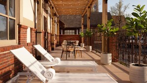 A covered outdoor seating area with lounge chairs and tables, brick walls, and potted plants.