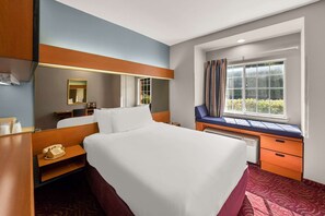 A hotel room with a large bed, a desk with a chair, a window with curtains, a mirror, and a telephone on a nightstand.