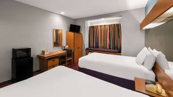 Habitación de hotel con cama, escritorio con computadora, televisor y ventana con cortinas.