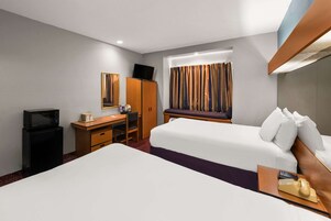 Habitación de hotel con cama, escritorio con computadora, televisor y ventana con cortinas.