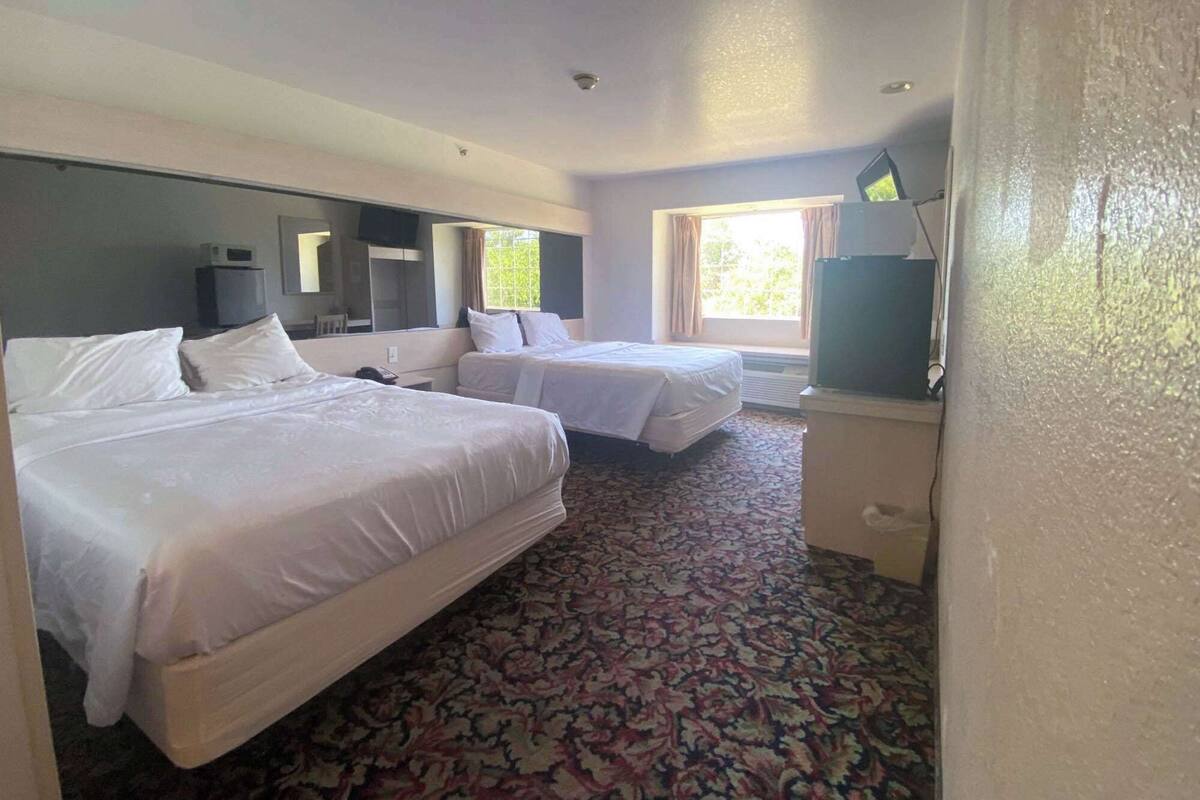 A hotel room with two beds, a large window, a flat-screen TV, and a patterned carpet.