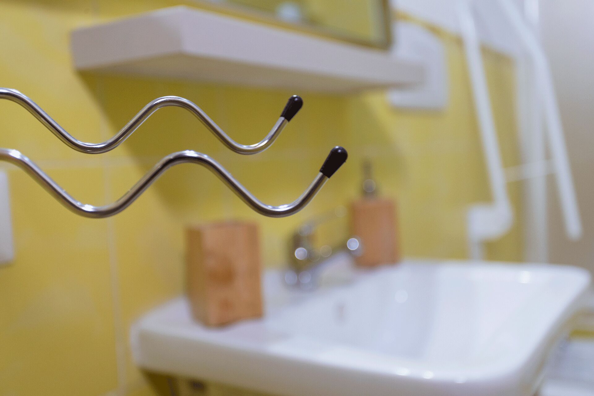 A bathroom with a white sink, yellow walls, and a metal towel rack.