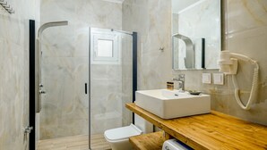 Un bagno moderno con cabina doccia in vetro, lavandino bianco e mobile contenitore in legno.