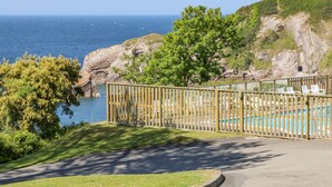 Un espace piscine agrémenté d’une clôture en bois, de chaises et offrant une vue sur la mer.