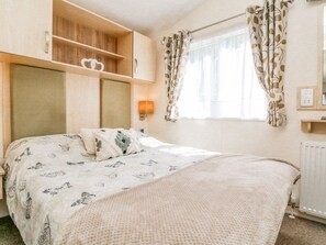 Un dormitorio con cama, mesita de noche, lámpara, armario y ventana con cortinas.