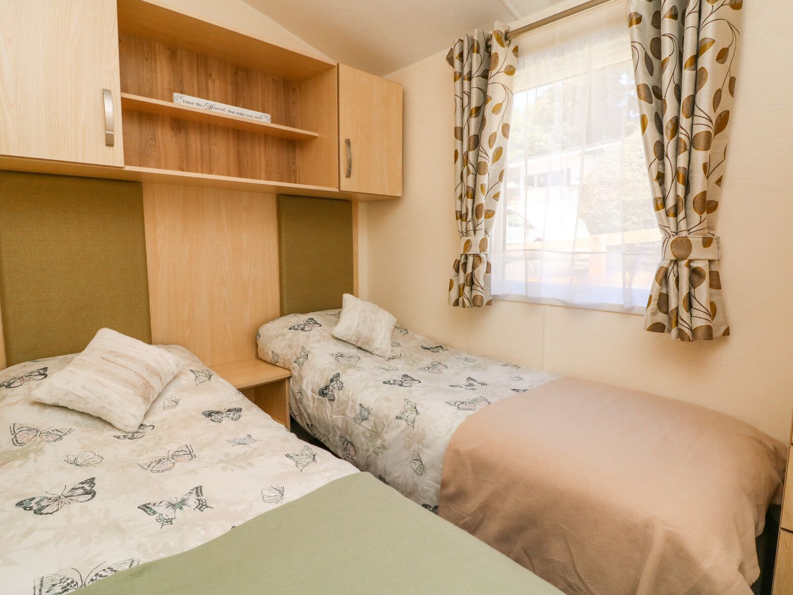 A room with two single beds, a wooden cabinet, and a window with leaf-patterned curtains.