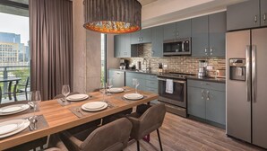 A modern kitchen with grey cabinets, a stainless steel refrigerator, and a dining area with a wooden table set for four.