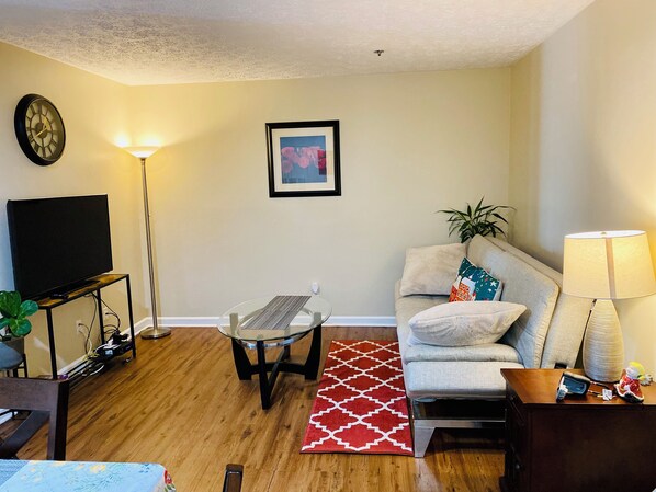 A living room with a flat-screen TV, a glass coffee table, a sofa, a red patterned rug, and a lamp. - Midtown 2BR/2BA Long-Term near Vandy/St.Thomas (Nashville)