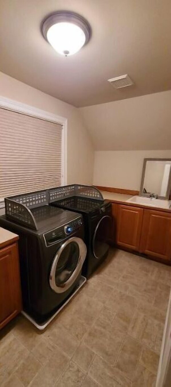 A laundry room with a washing machine and dryer, wooden cabinets, a tiled floor, and a window with blinds.