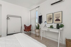 A bedroom with a bed, a desk, a chair, a hanging plant, and wall art.