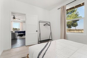 Un dormitorio con cama, perchero, puerta que da a un balcón y vistas a árboles.