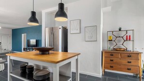 A modern kitchen with a wooden table, black pendant lights, a stainless steel refrigerator, and a wooden cabinet with drawers. - Desert Artist Oasis| Fire-pit | Spa | 5 min to JT, Desert Artist Oasis| Fire-pit | Spa | 5 min to (Yucca Valley)