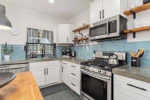 A modern kitchen with white cabinets, a gas stove, a microwave, and a coffee maker.