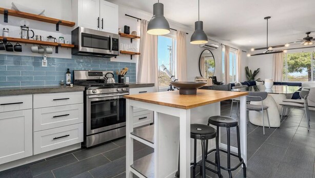 A modern kitchen with white cabinets, a stainless steel stove, and a large island with stools. - Desert Artist Oasis| Fire-pit | Spa | 5 min to JT, Desert Artist Oasis| Fire-pit | Spa | 5 min to (Yucca Valley)