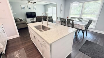 A modern kitchen with a central island, a dining area with a table and chairs, and a living room with a sofa and TV.