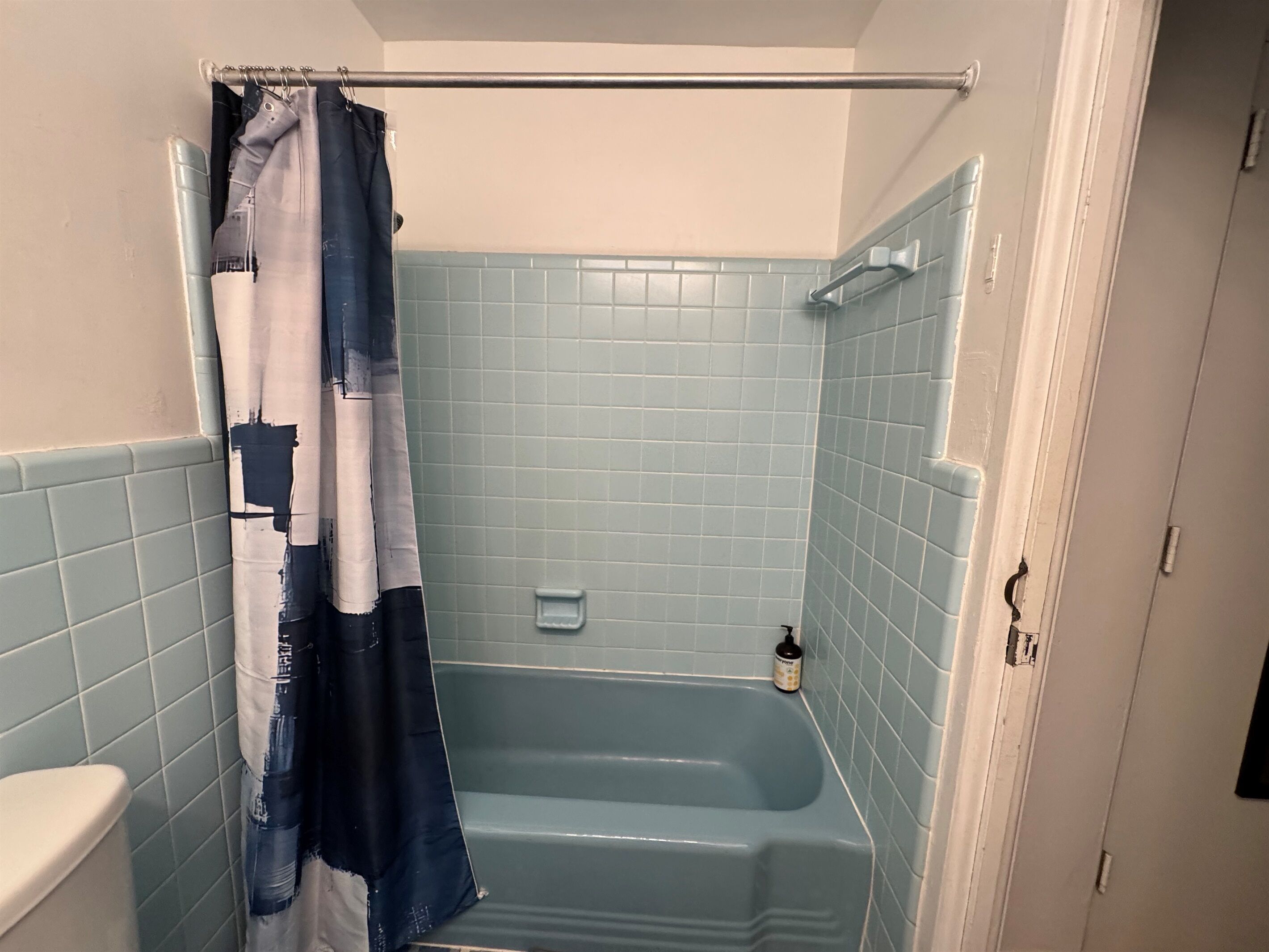 A bathroom with a blue-tiled shower area, a white toilet, and a door leading to another room.