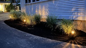 Uma casa com entrada por uma calçada, um jardim bem cuidado com gramado e um caminho iluminado.